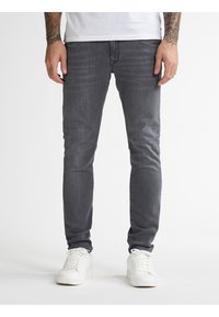 Jeans ajustados grises de denim, con un acabado desgastado y un sutil efecto de arrugas. Combinados con zapatillas blancas para un look informal.