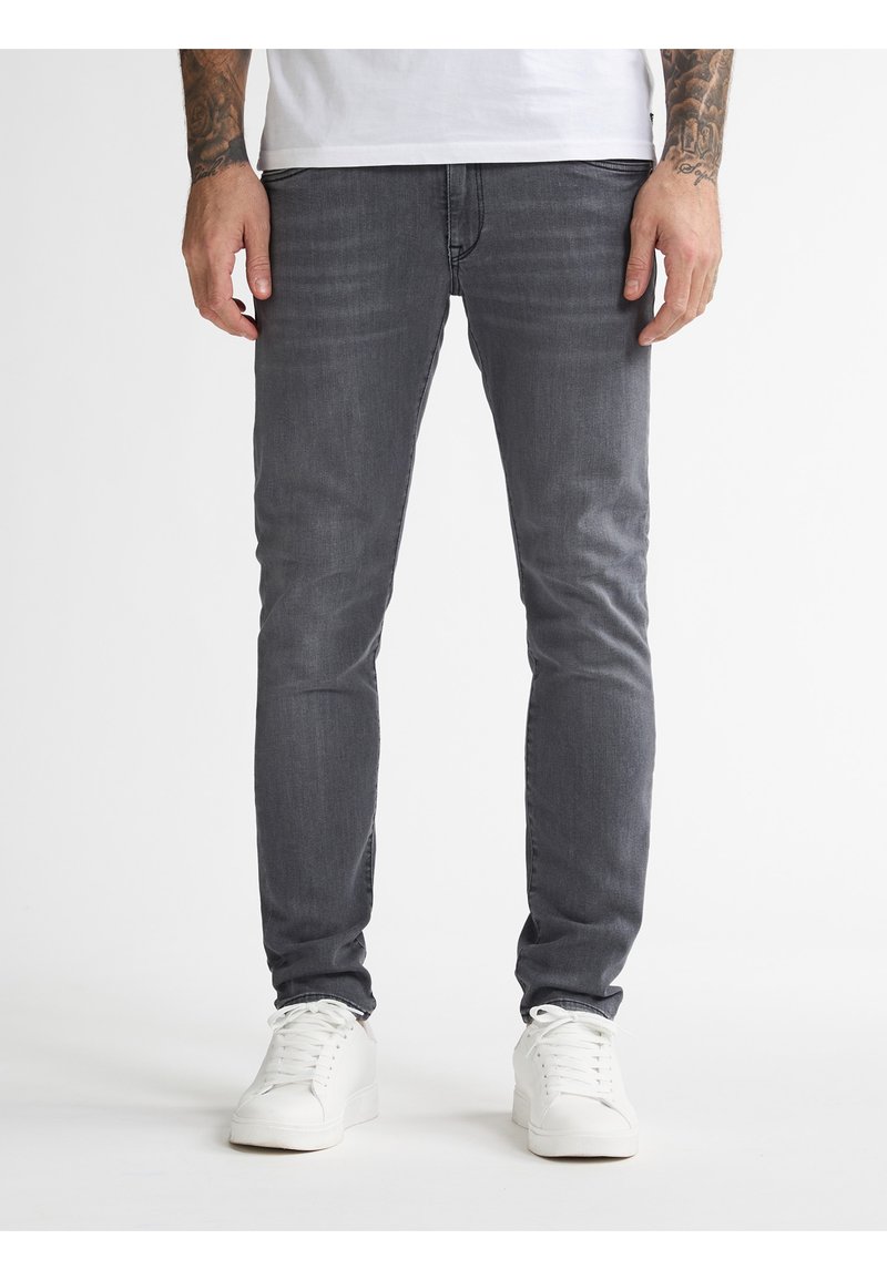 Jeans ajustados grises de denim, con un acabado desgastado y un sutil efecto de arrugas. Combinados con zapatillas blancas para un look informal.