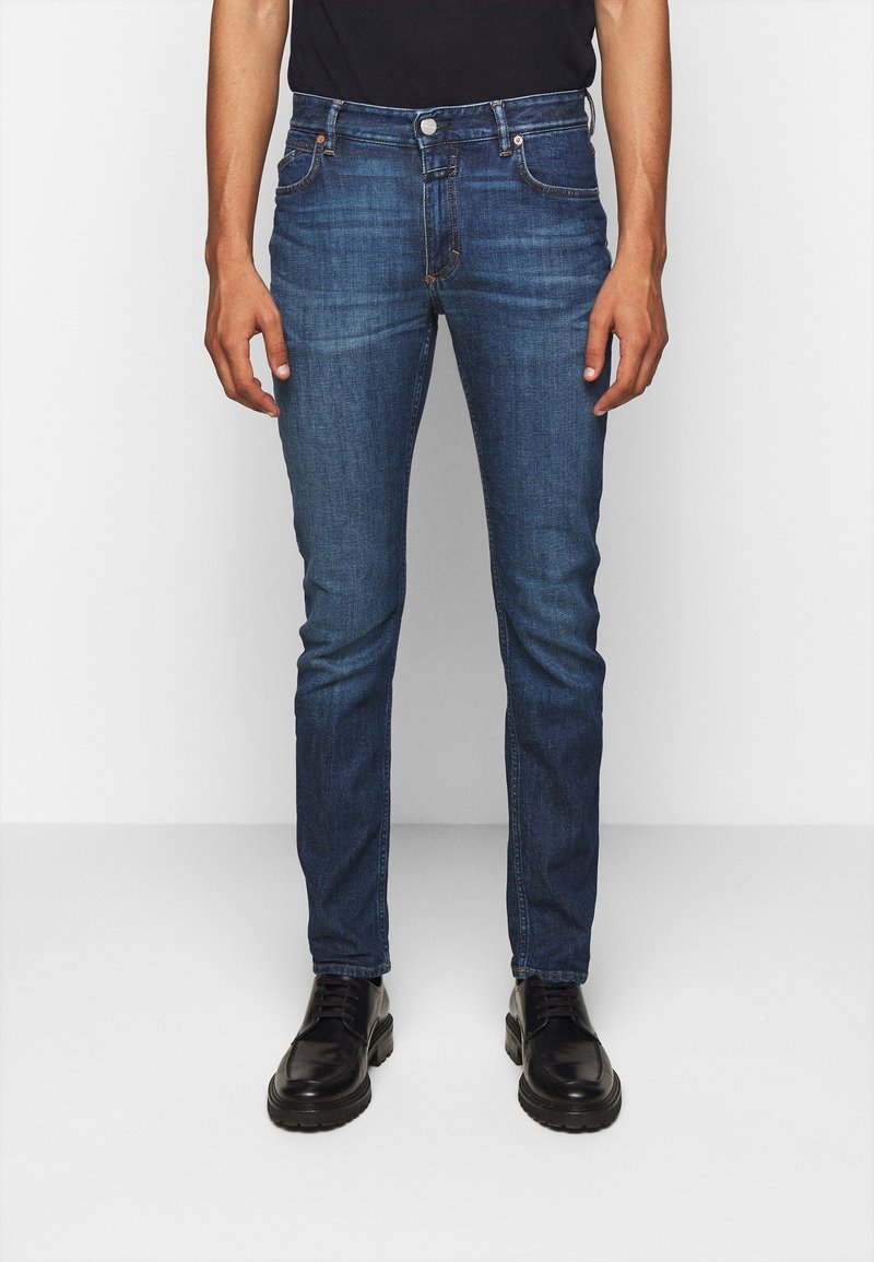 Jeans in denim blu slim fit con texture usurata, design a cinque tasche e cuciture a contrasto. Abbinati a scarpe nere stringate.