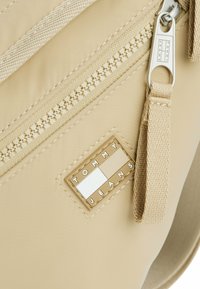Borsa in nylon beige con una cerniera prominente, una tracolla texture e un logo rettangolare Tommy Jeans con accenti geometrici.