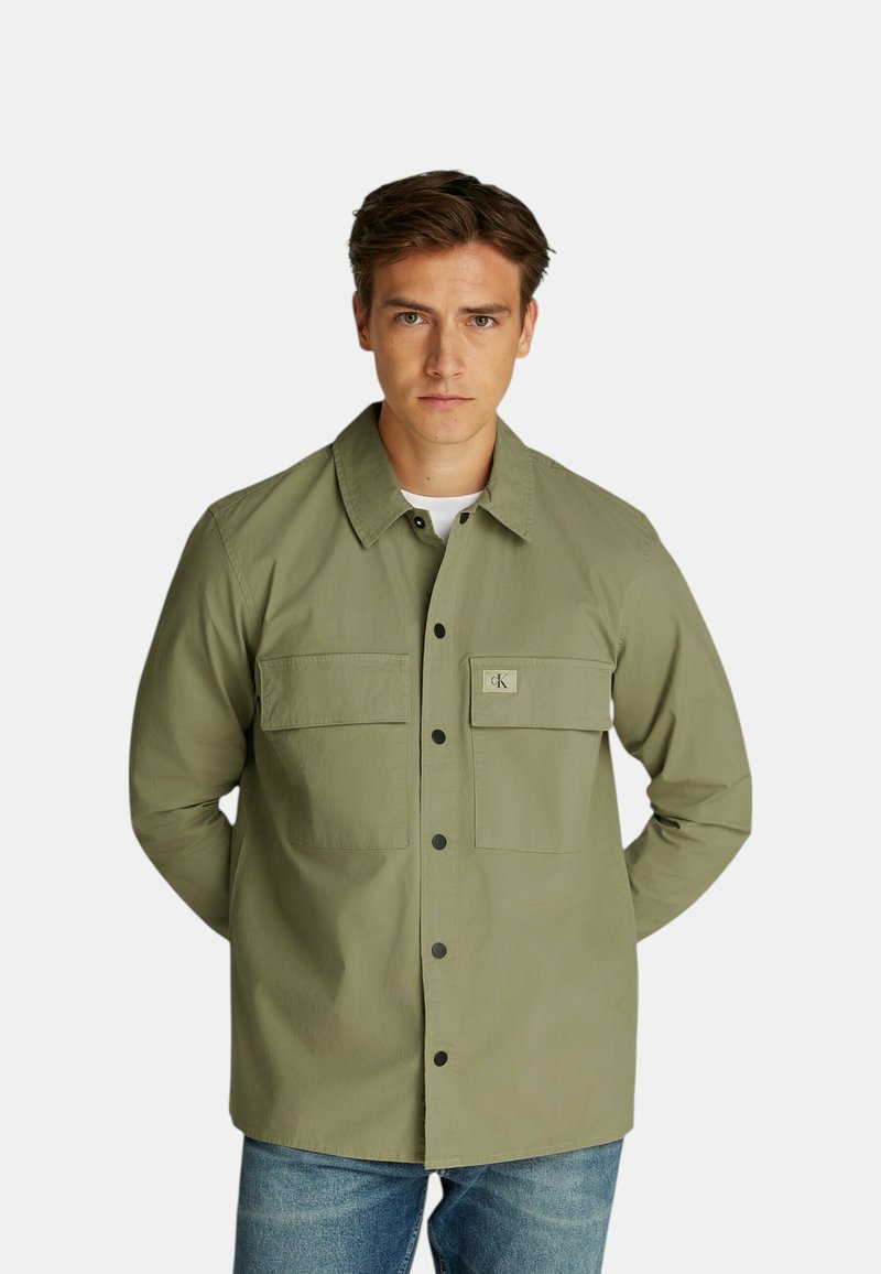 Camicia verde oliva in cotone con taglio rilassato, dotata di due tasche sul petto e un piccolo logo sulla tasca sinistra.