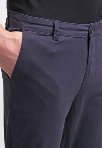 Mörkblå byxor i en slät bomullstyg, med platt front, sidfickor och en knappstängning.