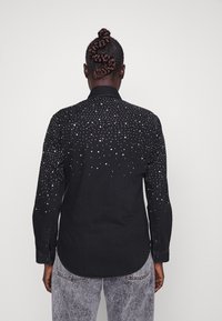 Black denim shirt featuring silver embellishments in a gradient pattern from top to bottom, with a button-down collar and long sleeves.