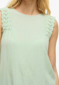 Jasnozielony top bez rękawów z koronkowymi akcentami na ramionach, miękką fakturą i luźnym krojem z okrągłym dekoltem.