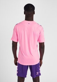 Helles pinkes kurzärmliges Sportshirt mit Rundhalsausschnitt. Weiche Textur und kontrastierende dunkle Akzente an den Schultern. Gewählt mit lila Shorts.