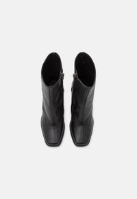 Ett par svarta läderankelboots med fyrkantiga tår och sidodragkedjor, visade ovanifrån på en enfärgad vit bakgrund.