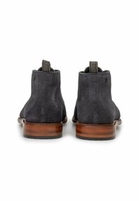 Par de botas de tobillo de cuero texturizado oscuro con tacones apilados marrones, vistas desde atrás sobre un fondo blanco.