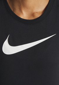 Camiseta negra de algodón con cuello redondo, que presenta un gran logo blanco de Nike en forma de swoosh ubicado en el centro. Textura suave, ajuste estándar.