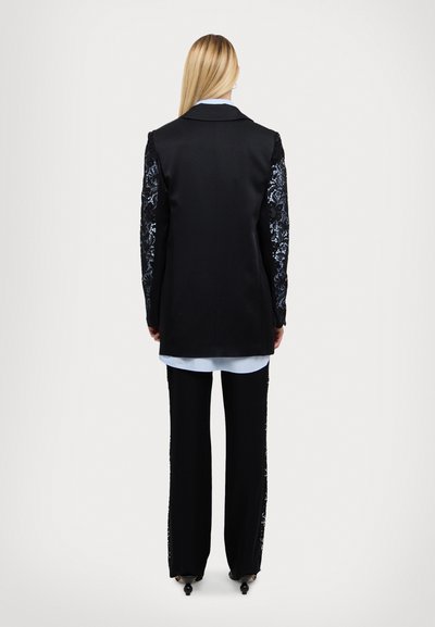 Black blazer with lace detail on sleeves, paired with a light blue shirt and black trousers. Smooth texture, tailored fit, elegant design.