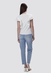 Hvid kortærmet skjorte med ruffle-detaljer på skuldrene, parret med lyseblå jeans og strappy hvide højhælede sandaler.