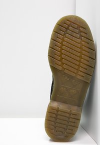 Suela de zapato de goma negra con un diseño texturizado y en patrón. Incluye una banda de rodadura circular y rectangular, detalles del logo y un borde liso.