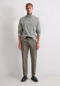 Jasnoszary sweter z zamkiem przy szyi, beżowe spodnie, czarny pasek i czarne buty. Sweter ma ściągacze na mankietach; spodnie są dopasowane o gładkiej fakturze.