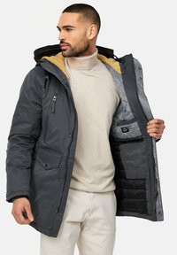 Parka gris aislante con capucha, que presenta un forro amarillo en contraste, cierres de cremallera y botones a presión, y múltiples bolsillos.