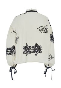 Blusa color crema con stampa floreale nera, maniche a sbuffo, scollatura con rouches e lacci alle estremità delle maniche. Design a vestibilità ampia e rilassata.