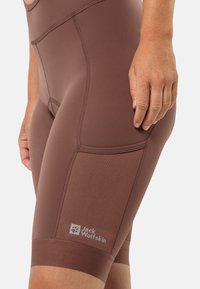 Bruine sportshorts met een getailleerd ontwerp, geprofileerde zijpanelen en een logo-patch. Gemaakt van rekbare, vochtregulerende stof.