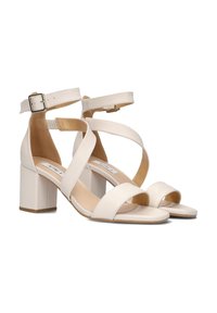 Blokhak sandalen in romig wit, met een breed kruisbandontwerp en een verstelbare enkelband met metalen gespsluiting. Gladde leertextuur.