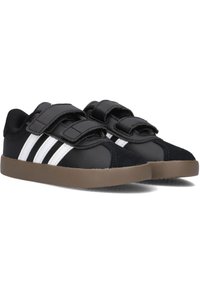 Černé tenisky se třemi bílými pruhy, vyrobené z kombinace kožených a textilních materiálů, s suchými zipy a hnědou gumovou podrážkou.