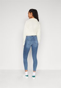 Suéter ligero de punto blanco combinado con unos jeans de mezclilla ajustados de color azul. Los jeans presentan un diseño clásico de cinco bolsillos y un desvanecimiento sutil.