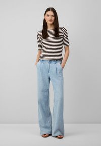 Haut à manches courtes rayé marron et crème associé à un jean large bleu clair, avec poches avant et coupe décontractée.