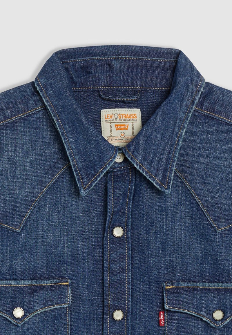 Camisa de mezclilla con cuello tipo punta, canesú al estilo western y dos bolsillos en el pecho. Color azul oscuro con costuras en contraste y botones de metal.