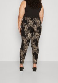 Svarta byxor med guldbladsmönster, figurnära design, slät textur, hög midja och en lätt stretch för komfort. Stilen kompletteras med högklackade skor.