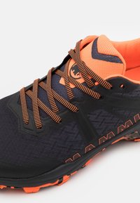 Black and orange athletic shoe featuring a textured upper, prominent lacing, and a solid rubber sole with orange accents and tread.