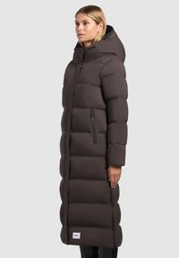Lange, donkerbruine pufferjas met een capuchon, met een gequilt ontwerp, zijzakken met rits en een merklabel aan de zoom.