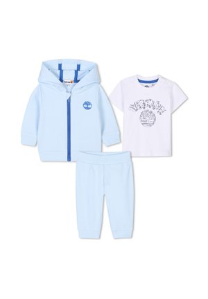 Ensemble de survêtement bleu clair avec une veste à fermeture éclair, t-shirt blanc avec un motif et un pantalon bleu assorti. Texture douce en coton sur l'ensemble.