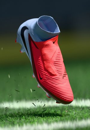 Nike soccer cleat in vibrant red and black, featuring a textured upper, ankle sock design, and multiple studs for traction on grass.