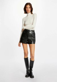 Zwarte leren hooggelegde shorts gecombineerd met een aansluitende crèmekleurige coltrui en kniehoge zwarte laarzen. De look heeft een minimalistisch ontwerp.