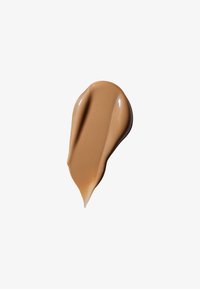 Fond de teint crémeux avec une teinte bronzée, texture lisse et légère brillance. Forme d'application tourbillonnée sur un fond blanc.