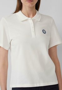 Weißes Poloshirt aus Baumwolle mit Kragen, fünfknöpfiger Knopfleiste, kurzen Ärmeln und einem runden Marine-Logo auf der Brust.