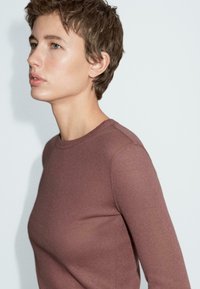 Langärmliges, tailliertes Oberteil in einem gedämpften Mauve-Farbton. Hergestellt aus weichem, geripptem Material mit einem klassischen Rundhalsausschnitt. Glatte Textur und nahtlose Schultern.