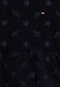 Dunkles Cordstoffgewebe mit bestickten Stern- und Blumenmustern in Marineblau und zarten Farbtönen, mit gerafften Details entlang des unteren Randes.