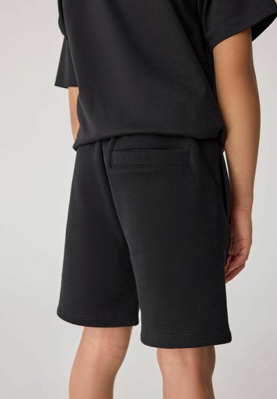 Svart bomullsskjorta med kort ärm och matchande shorts har en avslappnad passform, mjuk textur och en bakficka på shortsen.