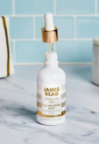 Bottiglia contagocce in vetro bianco con dettagli dorati e testo. Contiene 45 ml di gocce H2O per abbronzatura graduale per il corpo. Cappuccio contagocce trasparente.