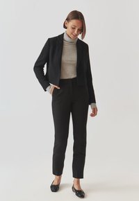 Crna skraćena blejzerica preko sive rolke, uparena s crnim tapered hlačama i ravnim crnim cipelicama. Glatka tkanina, krojena prilagodba, minimalistički dizajn.