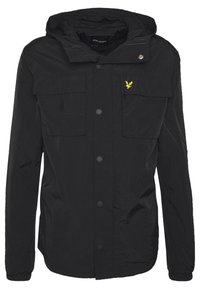 Musta hupullinen takki, jossa etupuolella painonapit, kaksi rintataskua läpillä, joustavat hihansuut ja vasemmassa taskussa pieni keltainen kirjailtu lintulogo.