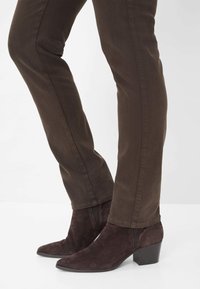 Donkerbruine suède enkellaarsjes met een spitse neus en een blokhak, gecombineerd met slanke, chocoladebruine broeken met een nette naad.