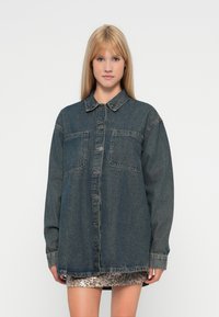 Temna modra denim srajca z dolgimi rokavi, zapenjanjem na gumbe spredaj, dvema žepoma na prsih in sproščenim, ohlapnim krojem. Mehka, teksturirana tkanina.