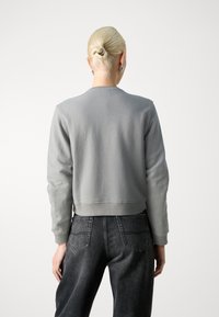 Sudadera gris corta con escote redondeado y puños acanalados, combinada con jeans de mezclilla oscura que tienen bolsillos traseros y una textura desgastada.