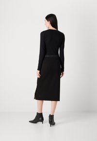 Top nero a maniche lunghe con un design aderente e scollatura rotonda, abbinato a una gonna nera con uno spacco laterale in stampa leopardata e stivaletti.