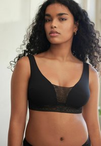 Reggiseno nero con tessuto liscio e rifinitura in pizzo al centro e al bordo inferiore. Spalline larghe e design con scollatura profonda.