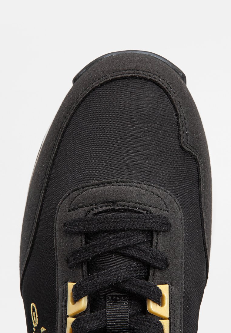 Svart sneaker med överdel i tyg och syntetmaterial, texturerade paneler, guldaccent hardware och svarta snören. Rund tådesign.