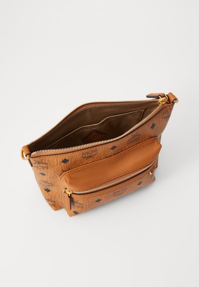 Tan läderhandväska med en texturerad yta, med ett zip-försett huvudfack och en extern ficka. Mönstrad med MCM-logotypen.