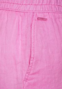 Rosa tyg med rynkad elastisk midja och sydd sidoficka med en liten rektangulär rosa etikett.