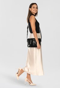 Borsa a spalla nera con texture a coccodrillo e accenti argentati, forma rettangolare e tracolla rimovibile, abbinata a un top nero e una gonna in satin crema.