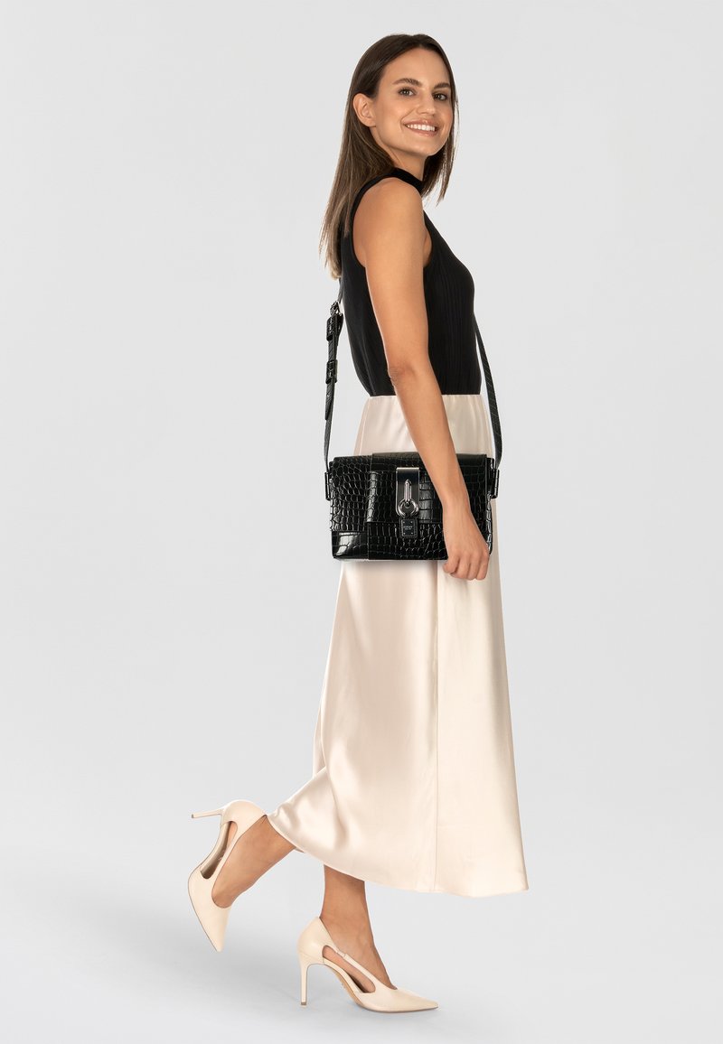 Borsa a spalla nera con texture a coccodrillo e accenti argentati, forma rettangolare e tracolla rimovibile, abbinata a un top nero e una gonna in satin crema.