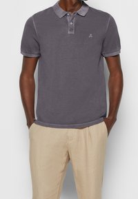 Koszulka polo w stonowanym odcieniu szarości, wykonana z bawełny, z kołnierzykiem, krótkimi rękawami oraz subtelnym haftowanym logo na piersi. Do kompletu jasnobeżowe spodnie.