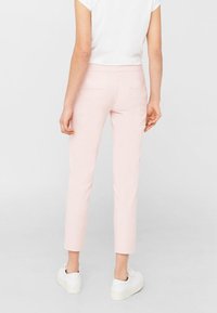 Pantalones ajustados de color rosa claro con un corte entallado, longitud corta y dos bolsillos traseros. Combinados con zapatillas blancas. Textura de tela suave.